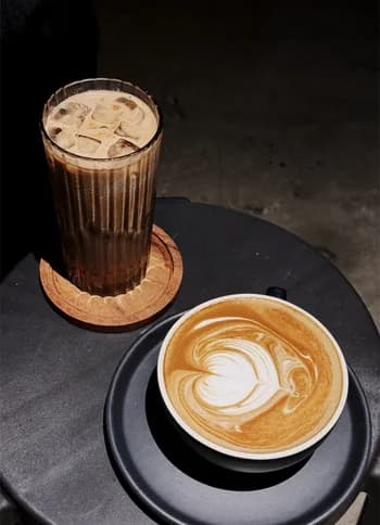 An iced coffee and a flat white on a dark cafe table