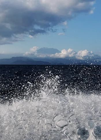 A wave breaking into spray, with clouds over a far shoreline