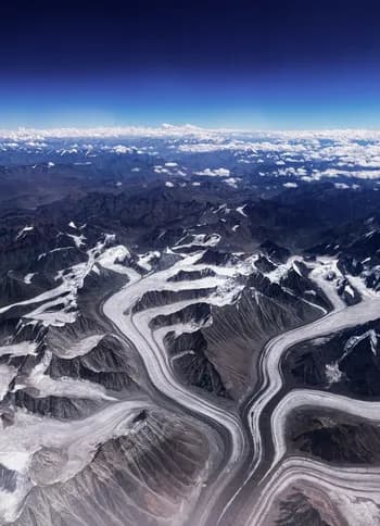 Glaciers winding between Himalayan ridges, seen from the air